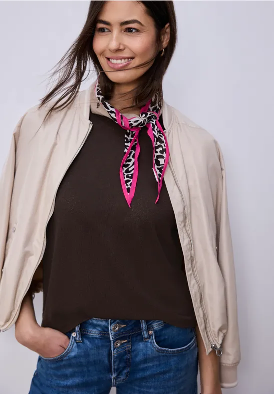 Personne porte un jean, un haut marron foncé, une veste beige et un foulard rose à motifs.