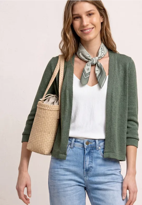 Vrouw in groen vest, wit topje en jeans, met halsdoek en rieten tas.