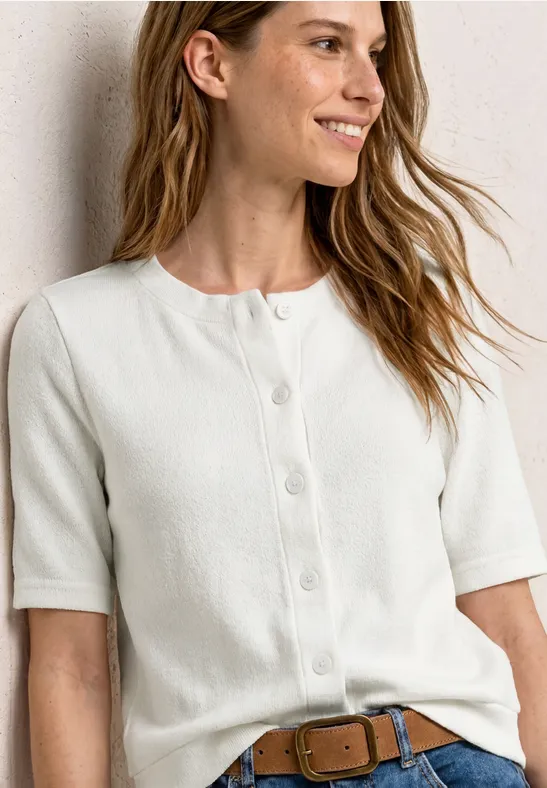 Vrouw draagt wit, kort gebreid vestje met knopen en korte mouwen, taillehoogte