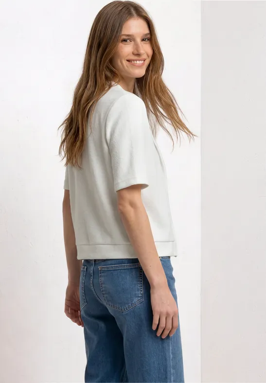 Een vrouw in een wit T-shirt en blauwe jeans, licht zijwaarts gezien.