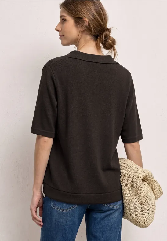 Vrouw van achteren in een donker polohemd, spijkerbroek en gevlochten tas