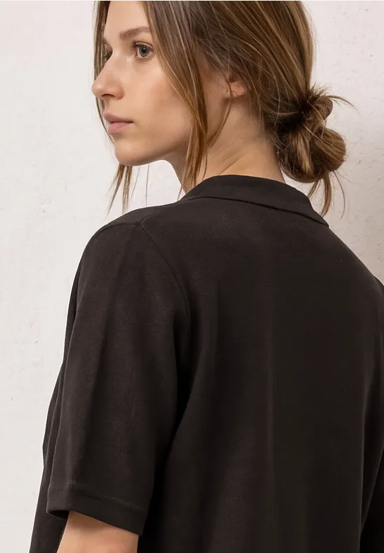 Jonge vrouw met samengebonden haar draagt een zwart T-shirt met korte mouwen en kijkt opzij.