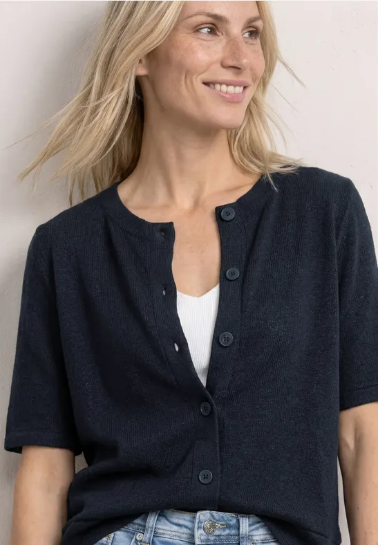 Blonde vrouw draagt een donkerblauwe korte mouw cardigan met knopen over een witte top.