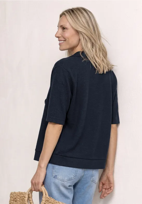 Persoon van achteren met een donkermarineblauw kort mouwtrui en lichtblauwe jeans, voor een eenvoudige achtergrond.