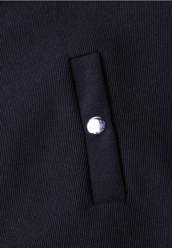Detail eines schwarzen Stoffes mit einer Leistentasche und einem silbernen Druckknopf.