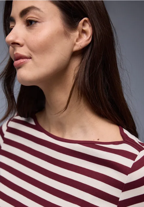 Frau mit schulterlangem braunem Haar in gestreiftem bordeaux-weißem Shirt, sichtbarer Hals.