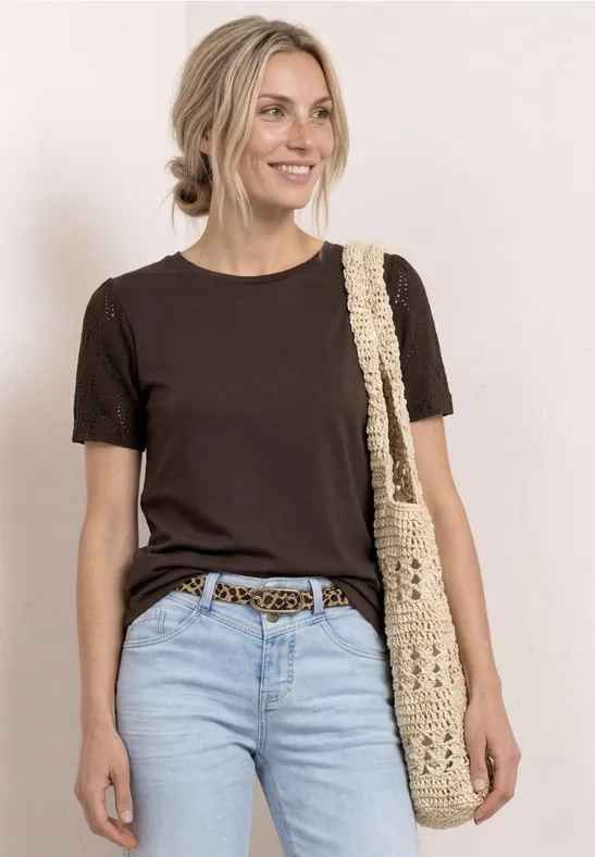 Frau trägt braunes T-Shirt, hellblaue Jeans, Leoparden-Taillengürtel und gehäkelte Tasche über der Schulter.