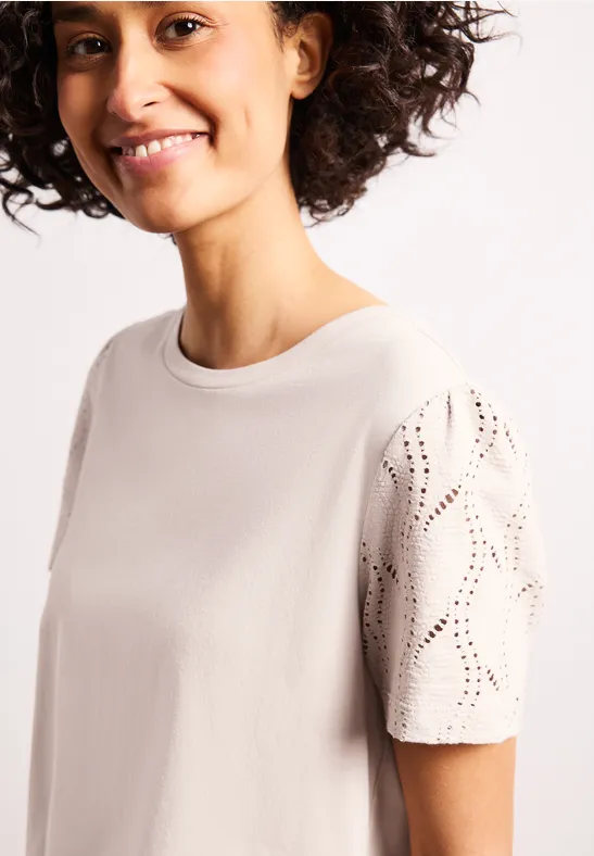 Beige T-shirt met ronde hals, geperforeerde mouwen en losse pasvorm.