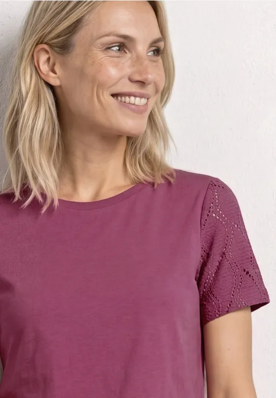 Lächelnde Frau in pflaumenfarbenem T-Shirt mit kurzen Ärmeln und feinen Spitzen-Details.