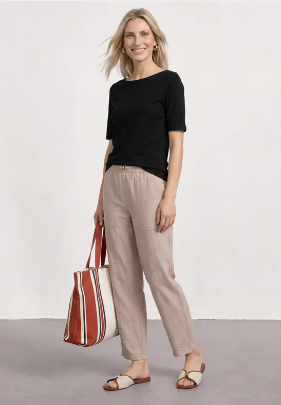 Femme en t-shirt noir, pantalon beige décontracté et sandales, portant un sac rayé rouge et blanc.