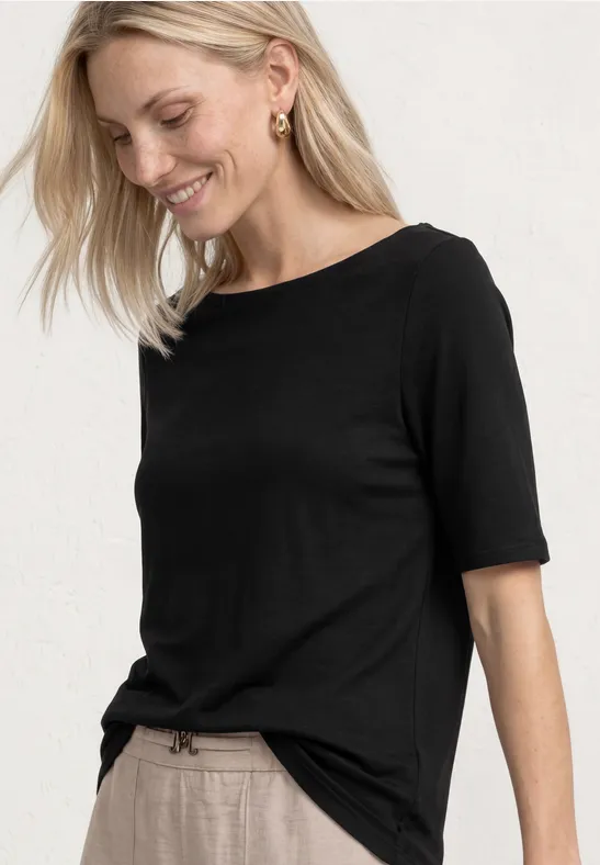 Modèle blond porte un t-shirt noir à manches courtes, partiellement rentré dans un pantalon clair.