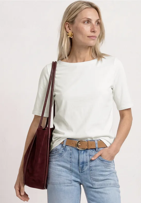 Femme en t-shirt blanc, jean bleu avec ceinture marron et sac épaule rouge.