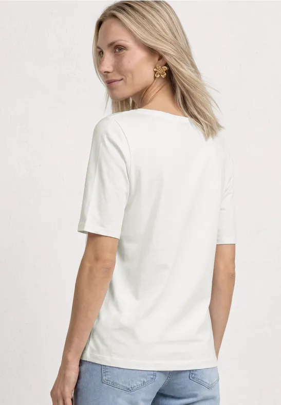 Une femme de dos en t-shirt blanc et jean clair sur un fond uni et lumineux.
