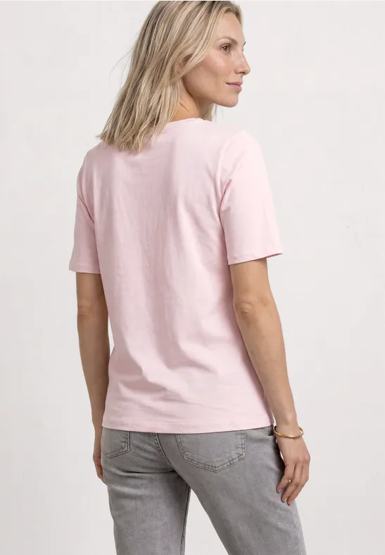 Rückansicht einer Frau, die ein pastellrosa T-Shirt und graue Jeans trägt.