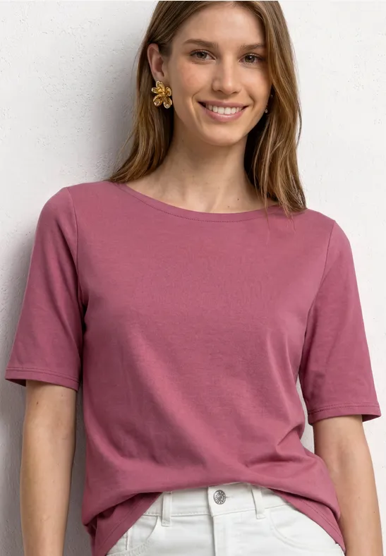 Eine Frau trägt ein rosafarbenes Kurzarmshirt und helle Jeans.