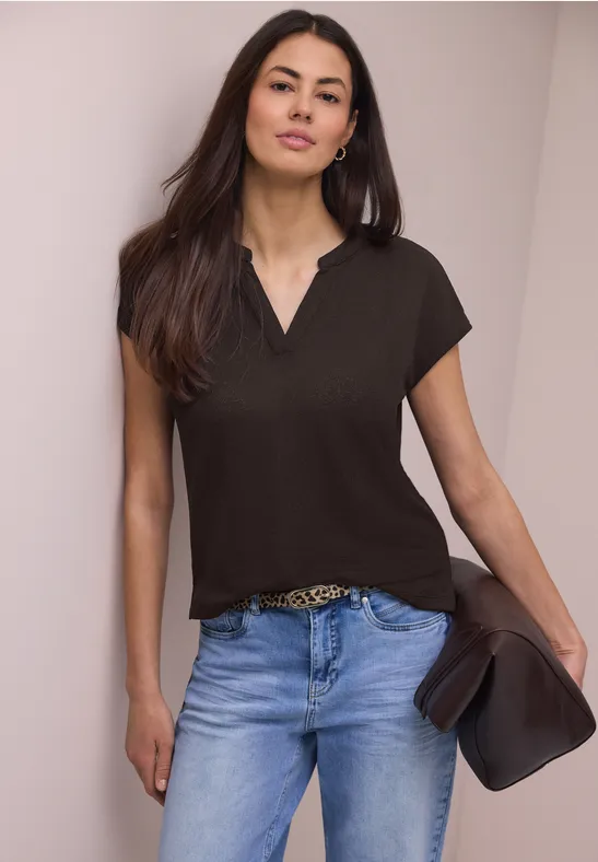 Eine Frau trägt ein schwarzes T-Shirt und helle Jeans, hält einen Hut in der Hand.