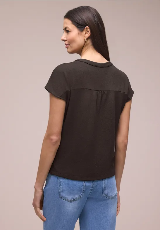 Frau von hinten in schlichtem schwarzen T-Shirt und blauen Jeans vor neutralem Hintergrund.