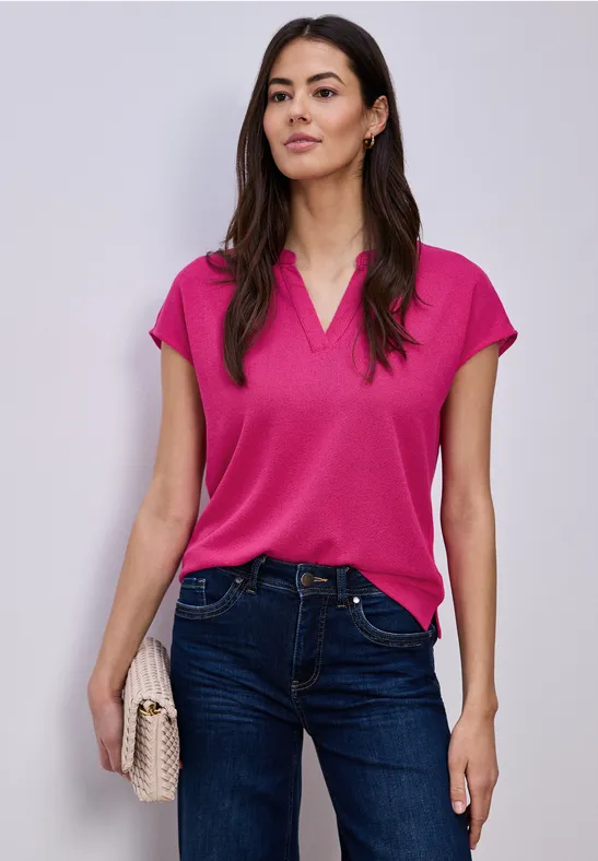 Frau in pinkem Oberteil, blauen Jeans und beiger Clutch vor weißem Hintergrund.