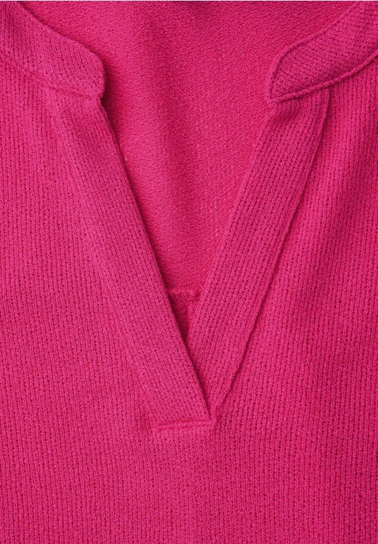Nahaufnahme eines fuchsiafarbenen, fein gestrickten Pullovers mit V-Ausschnitt.