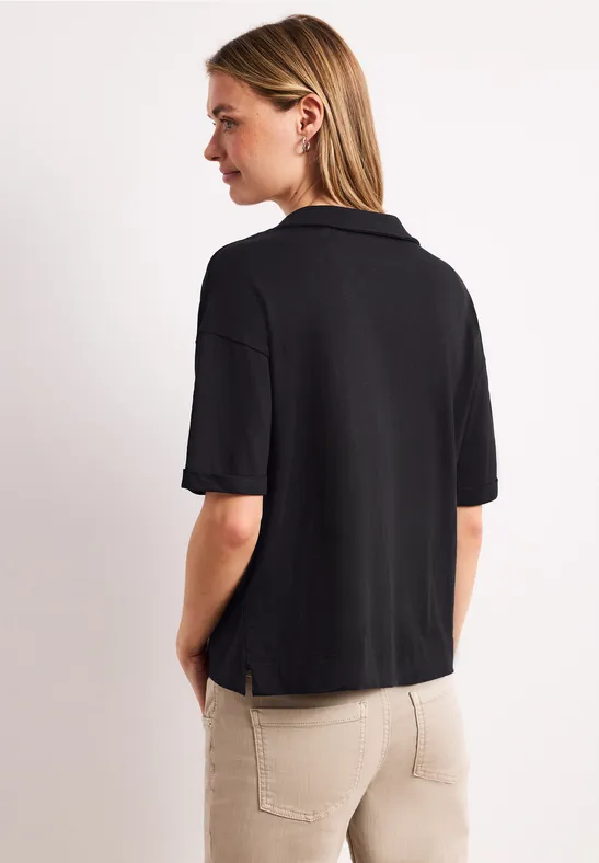 Eine Frau von hinten in schwarzem Poloshirt und heller Hose.