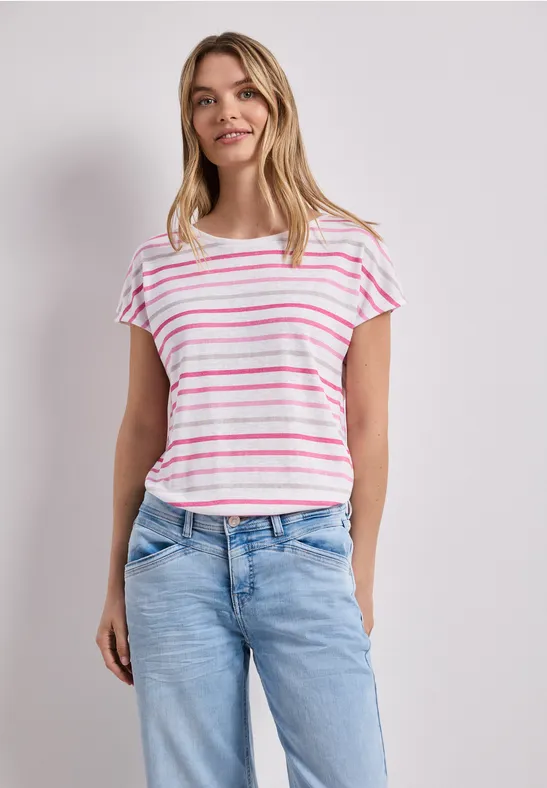 Femme portant un t-shirt blanc à rayures roses et un jean bleu sur fond uni.