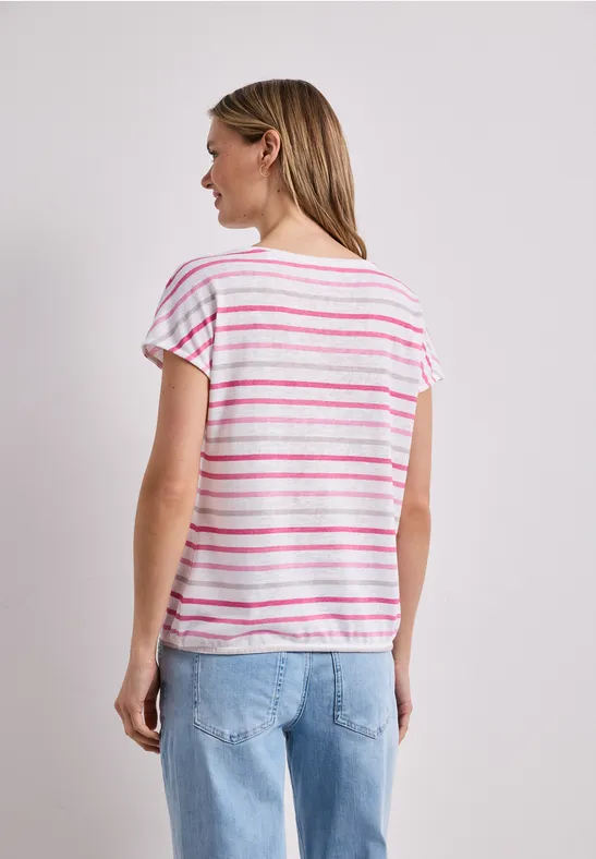 Femme de dos portant un T-shirt blanc à rayures roses et un jean bleu sur fond blanc.