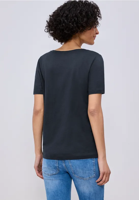 Person von hinten mit lockigem Haar, schwarzem T-Shirt und blauen Jeans.