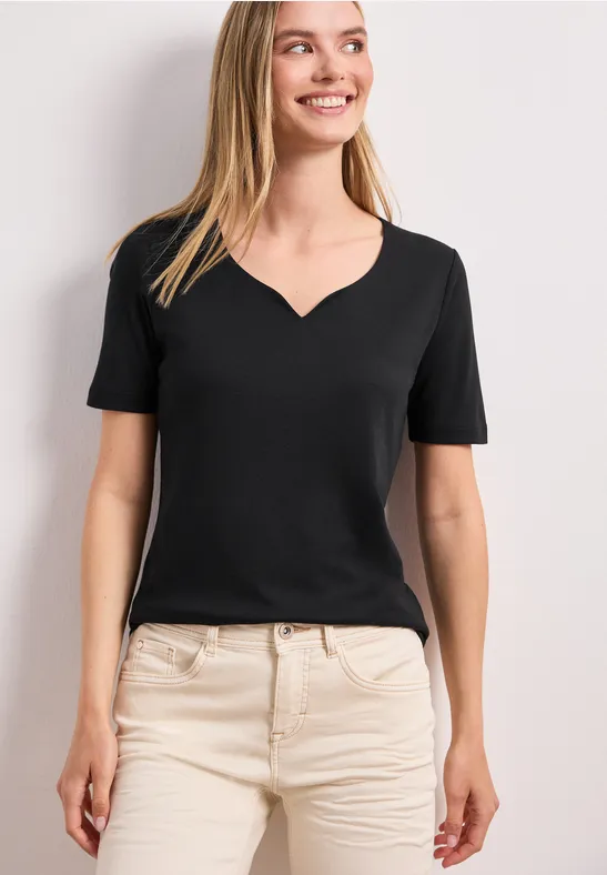 Vrouw in zwart V-hals T-shirt en beige broek tegen witte achtergrond.