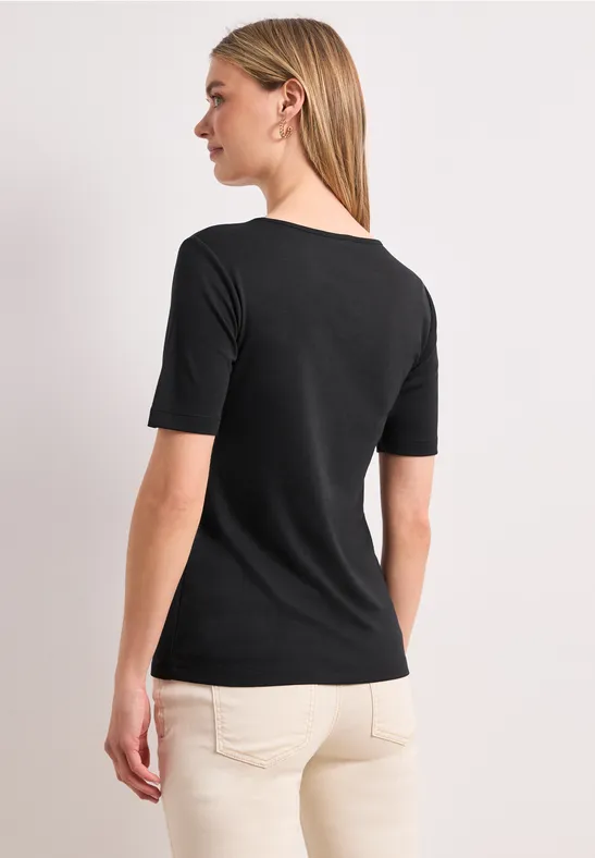 Blondine van achteren in een zwart shirt en beige broek tegen een lichte achtergrond.