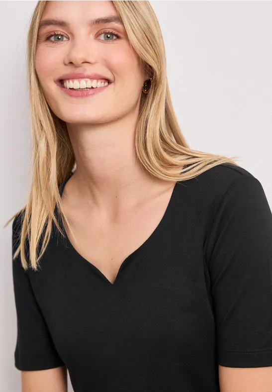 Vrouw met blond haar draagt een eenvoudig zwart T-shirt met V-hals.