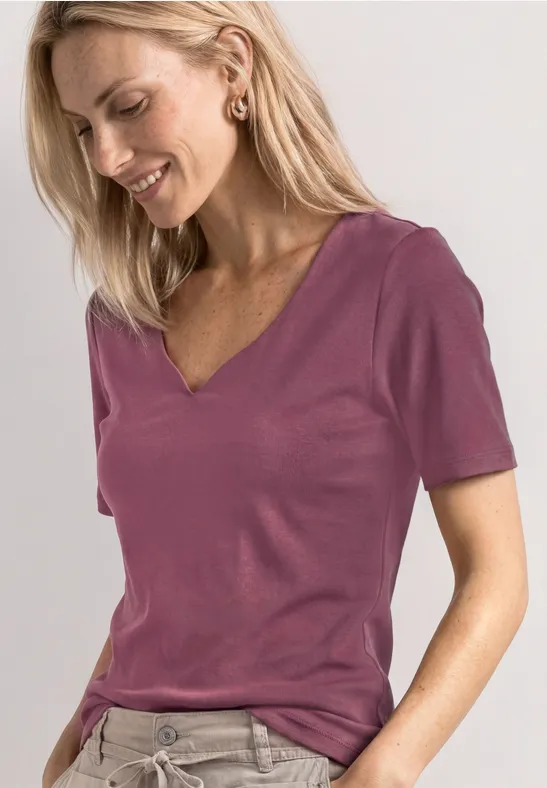 Femme blonde porte un t-shirt prune à col V, manches courtes, style décontracté.