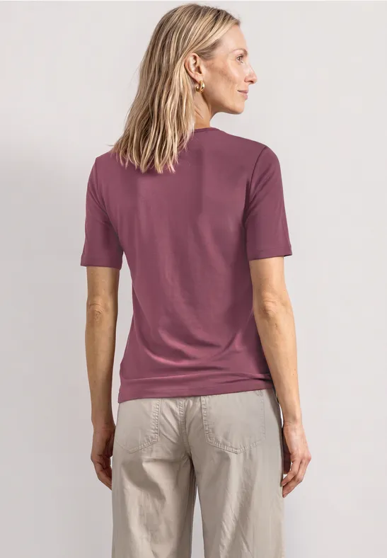 Femme de dos portant un t-shirt violet et un pantalon beige.