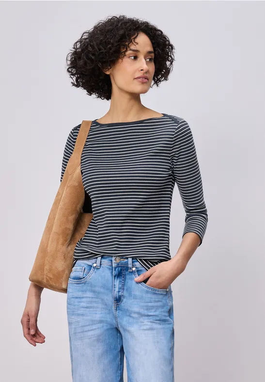 Eine Frau trägt ein gestreiftes 3/4-Arm-Shirt, blaue Jeans und eine hellbraune Schultertasche.
