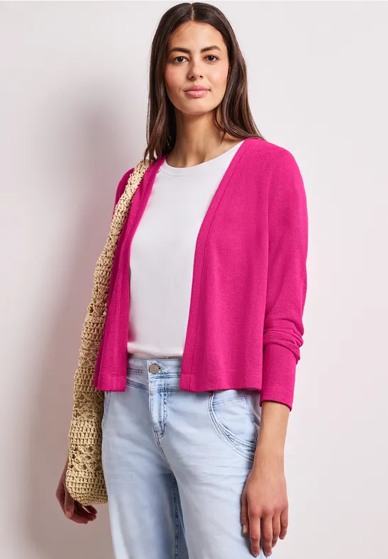 Vrouw met fuchsia vest, wit shirt, lichte spijkerbroek en strooien tas.