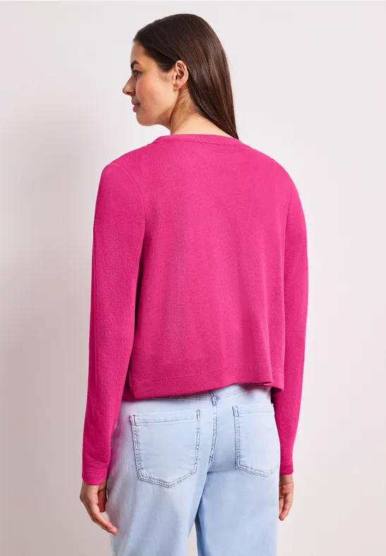 Vrouw van achteren in een felroze blazer en lichte jeans voor een neutrale achtergrond.
