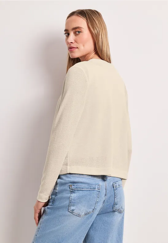 Vrouw draagt crèmekleurige trui en lichtblauwe jeans, rug naar de camera gekeerd.
