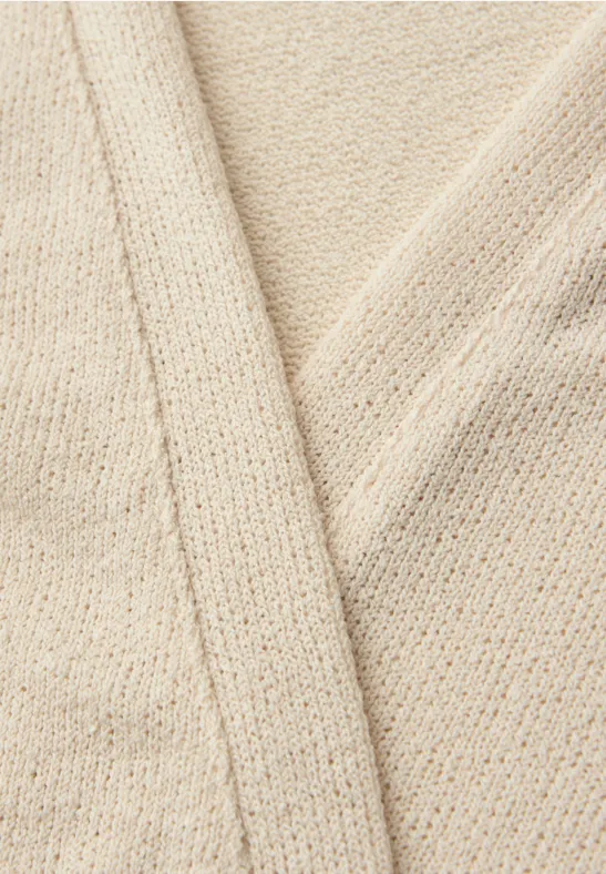 Close-up van een crèmekleurig, grof gebreid textiel met overlappende delen.
