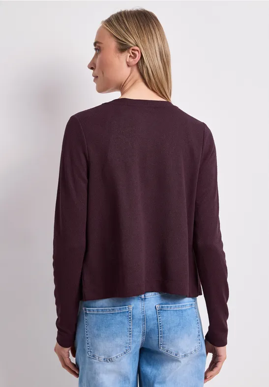 Vrouw van achteren in een donkerpaarse trui met lange mouwen en lichtblauwe jeans tegen neutrale achtergrond.