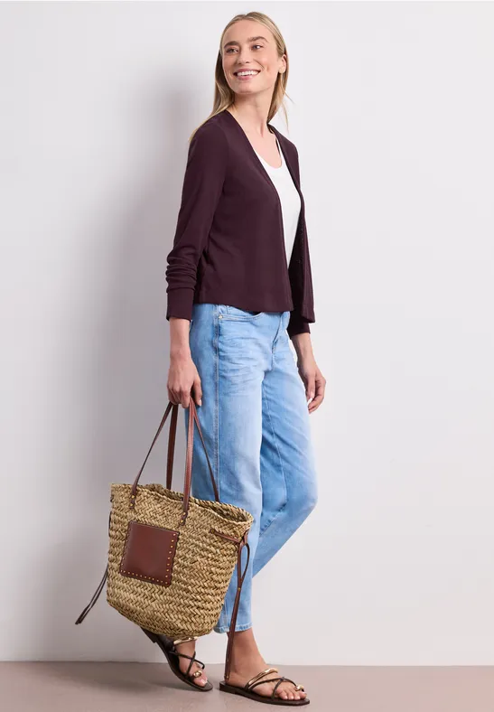 Vrouw in casual outfit met cardigan, wit shirt, blauwe jeans, sandalen en gevlochten tas.