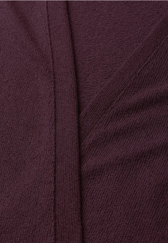 Close-up van bordeaux textiel met zichtbare naden en een opstaande plooi.