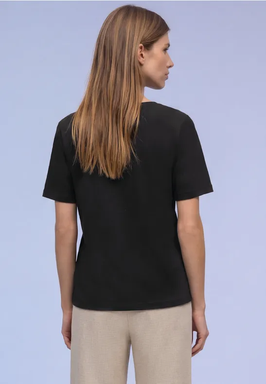 Eine Person mit schwarzem T-Shirt und beiger Hose, Rückenansicht vor lila Hintergrund.