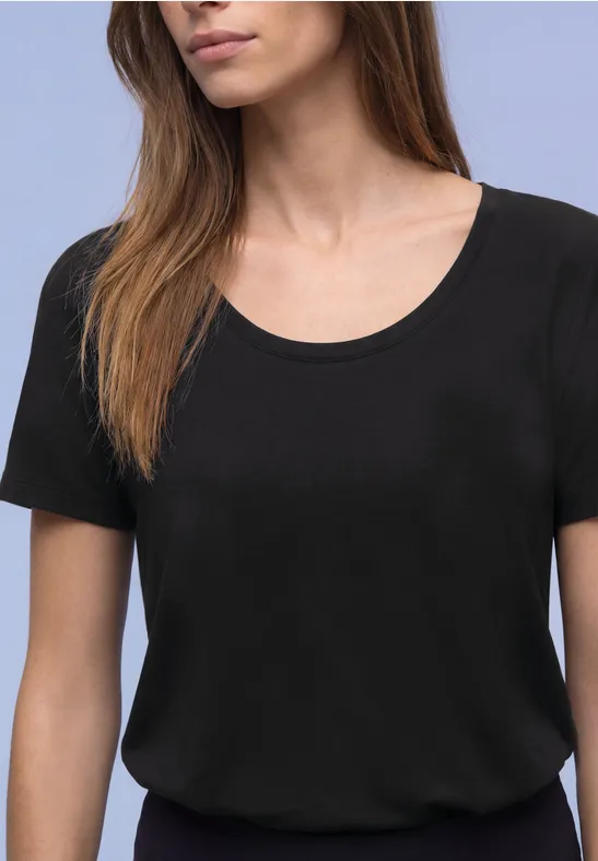 Eine Frau in schlichten, schwarzen Kurzarmshirt vor hellem Hintergrund.