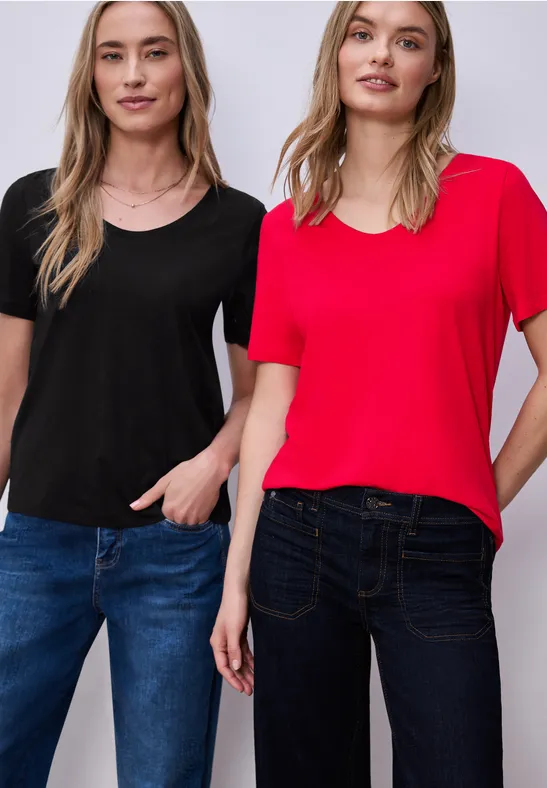 Zwei Personen stehen nebeneinander in Jeans und lässigen T-Shirts (schwarz und rot), eine Hand in der Hosentasche.