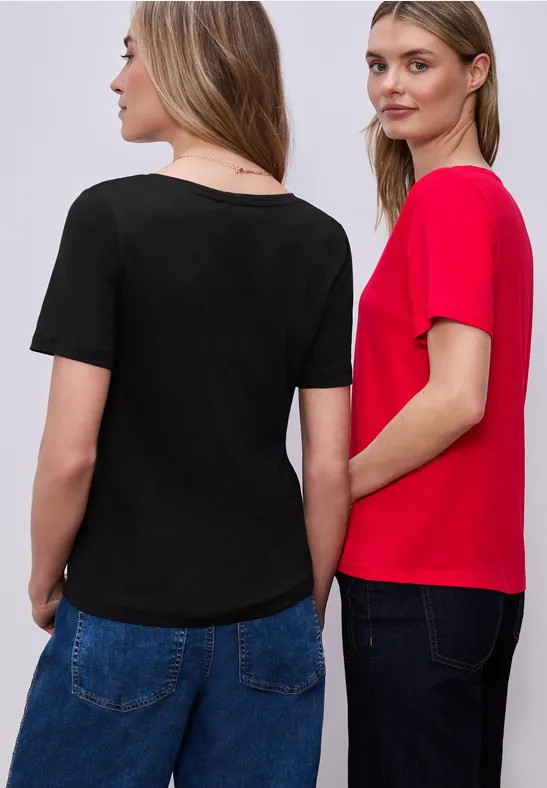Zwei Frauen in Jeans, eine im roten, die andere im schwarzen T-Shirt, stehen nebeneinander.