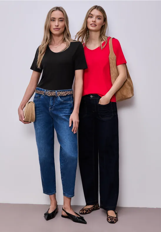 Zwei modebewusste Frauen in Jeans und T-Shirts posieren vor neutralem Hintergrund.