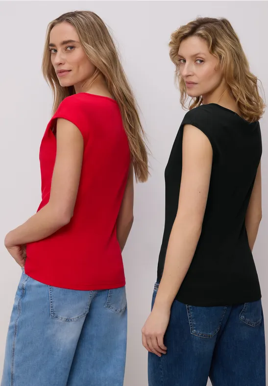 Zwei Frauen tragen bunte T-Shirts und Jeans, Seitenansicht vor weißem Hintergrund.