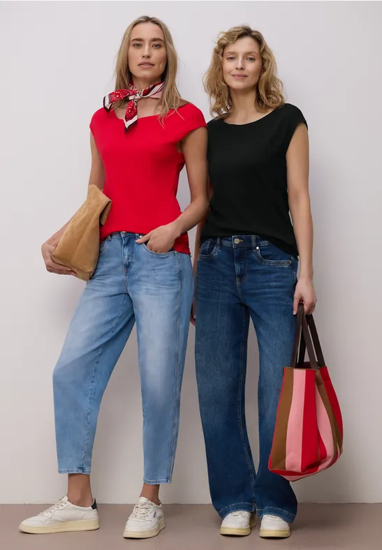 Zwei Frauen in lässiger Jeans und T-Shirt stehen nebeneinander, jede mit einer Umhängetasche.