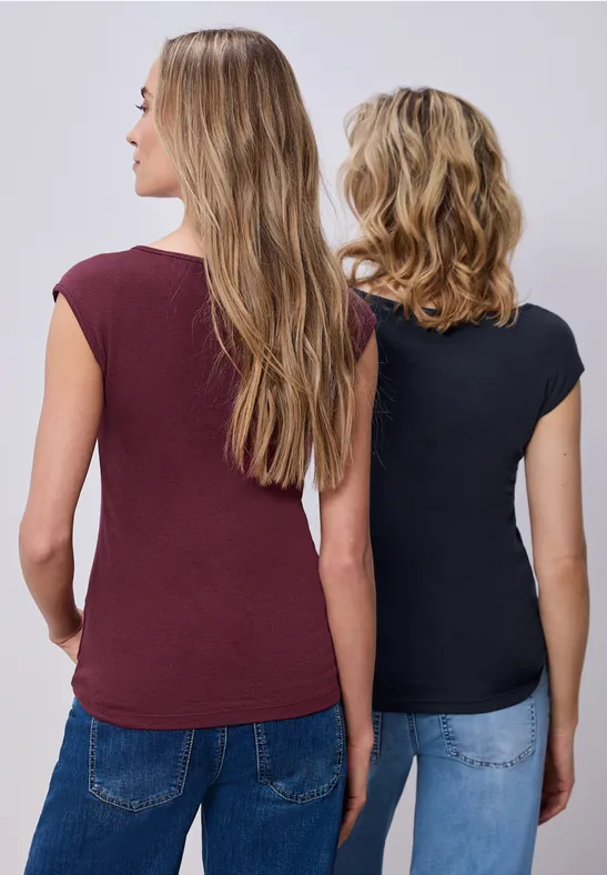 Zwei Frauen stehen nebeneinander, Rücken zur Kamera, tragen T-Shirts und Jeans.