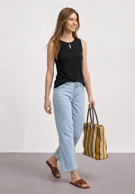 Eine Frau trägt schwarzes Top, helle Jeans, braune Sandalen und hält eine gestreifte Handtasche.