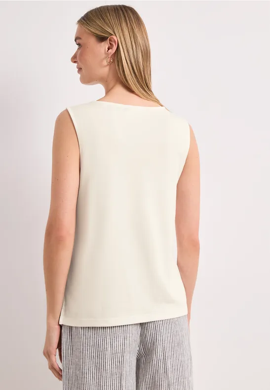 Frau von hinten in ärmellosem cremefarbenem Top und grauer Hose.